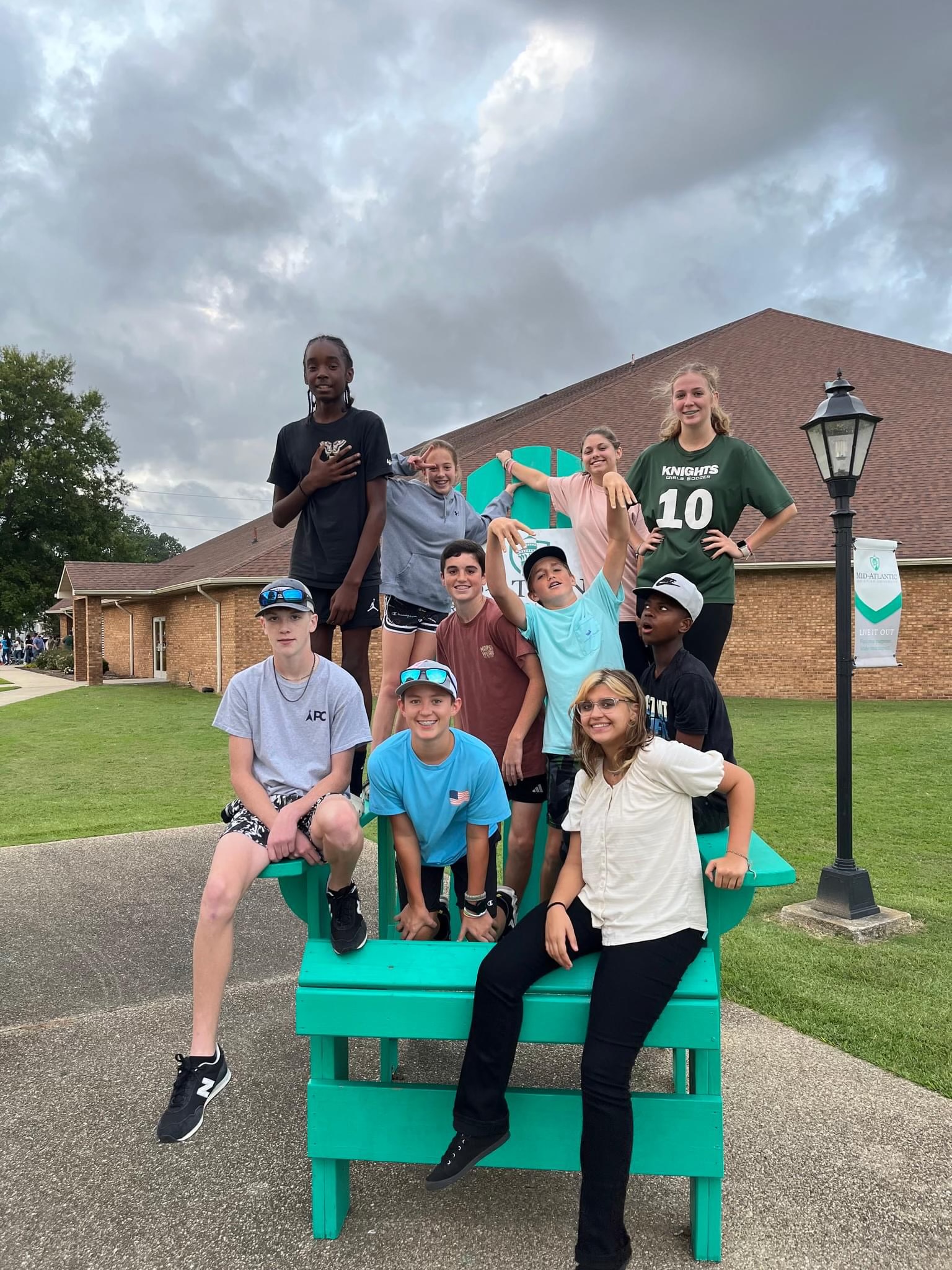 Youth Group sitting on a giant, green Adirondack chair at Mid-Atlantic Christian University.