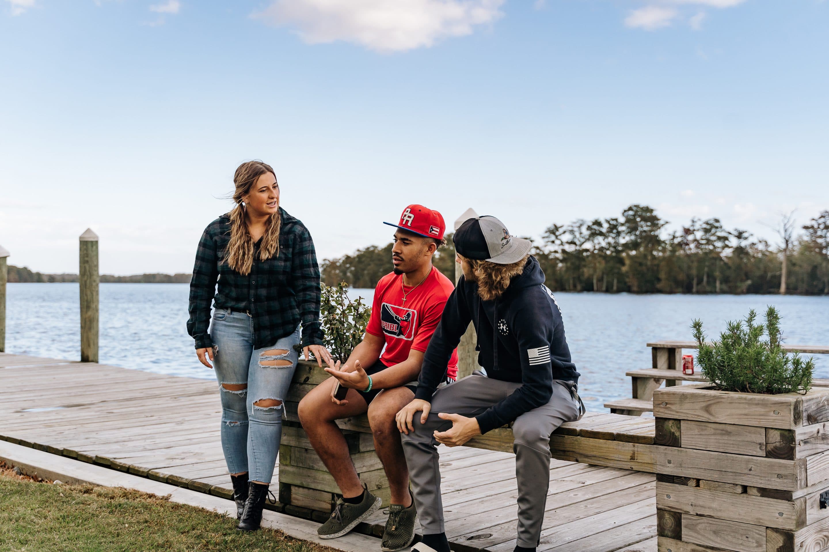Three students talking while sitting on the pier at a Christian college.